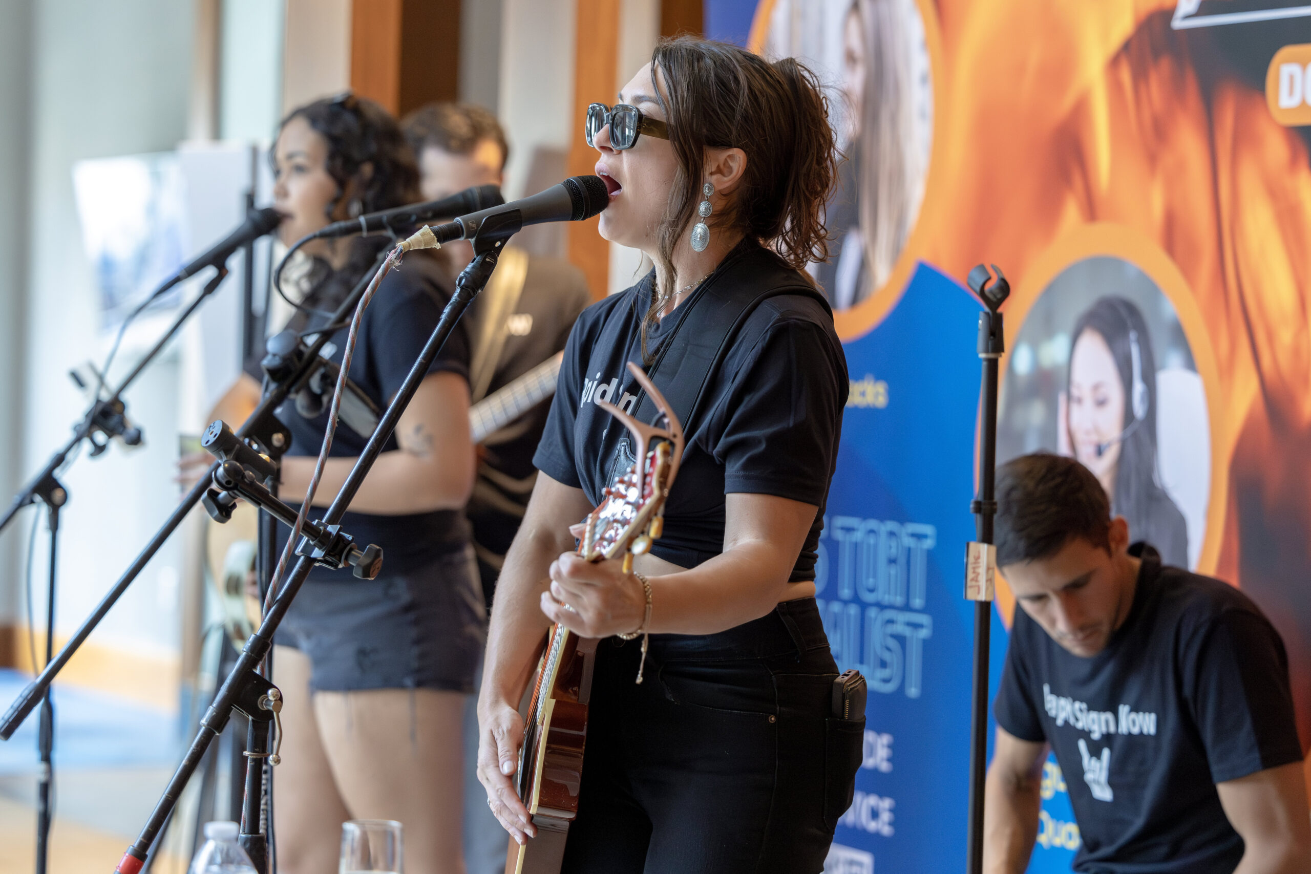 an image of a woman playing guitar with her bandmates at an event
