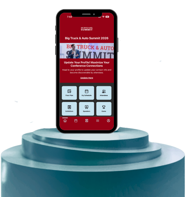 Smartphone mockup on a teal display podium showing the Big Truck & Auto Summit 2026 mobile app home screen with event navigation buttons and a profile update prompt.